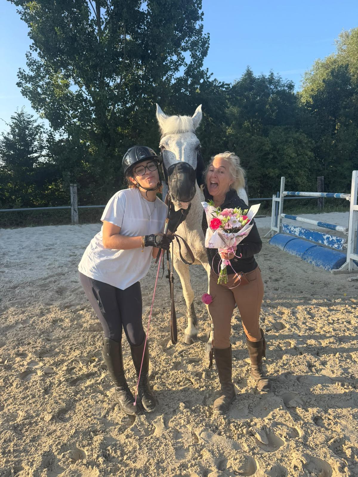 Deux personnes auprès d’un cheval gris dans une carrière équestre